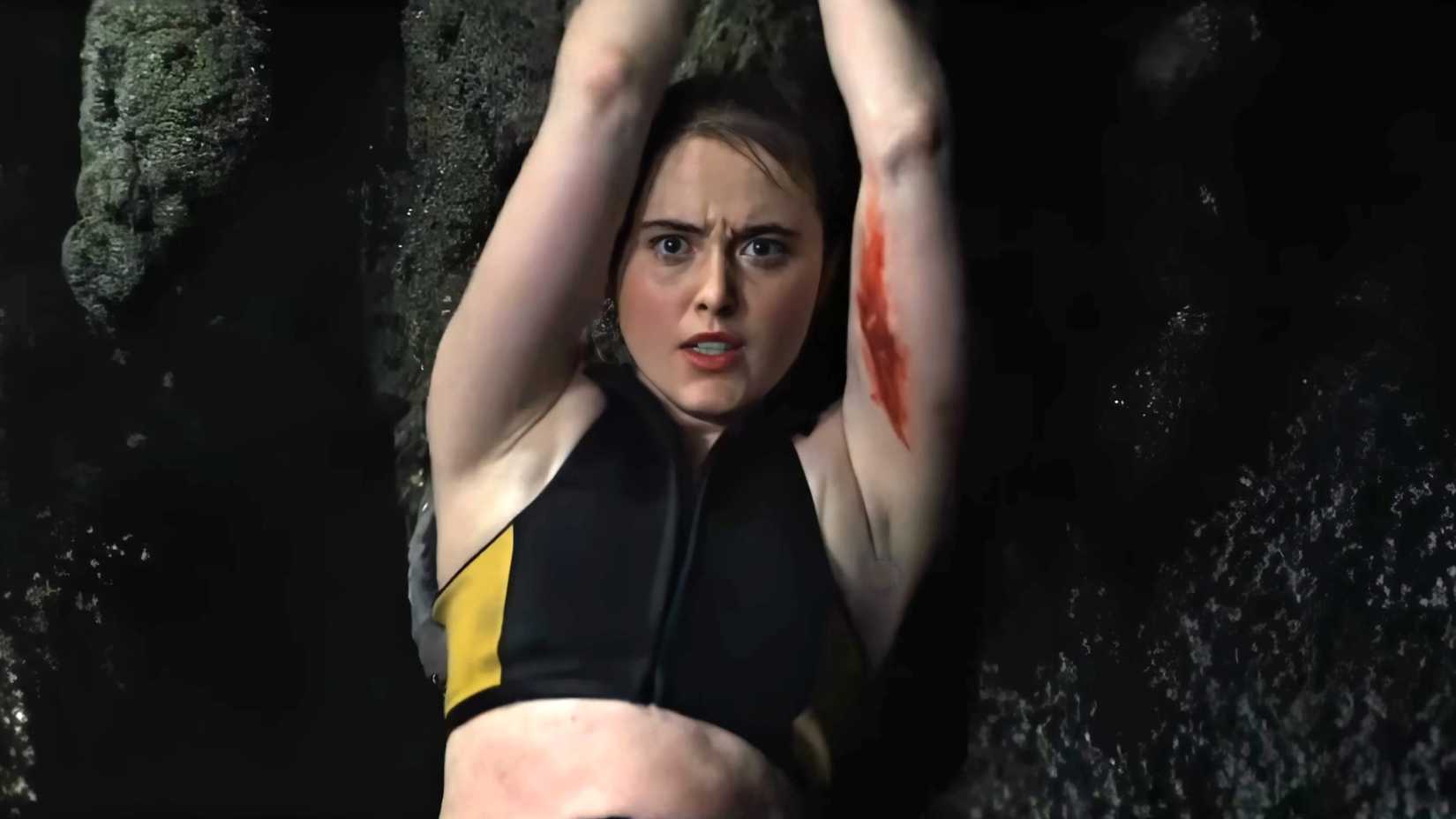 Kathryn Newton's Sara looking intensely while holding on to a rock and blood on her arm in The Devil's Mouth