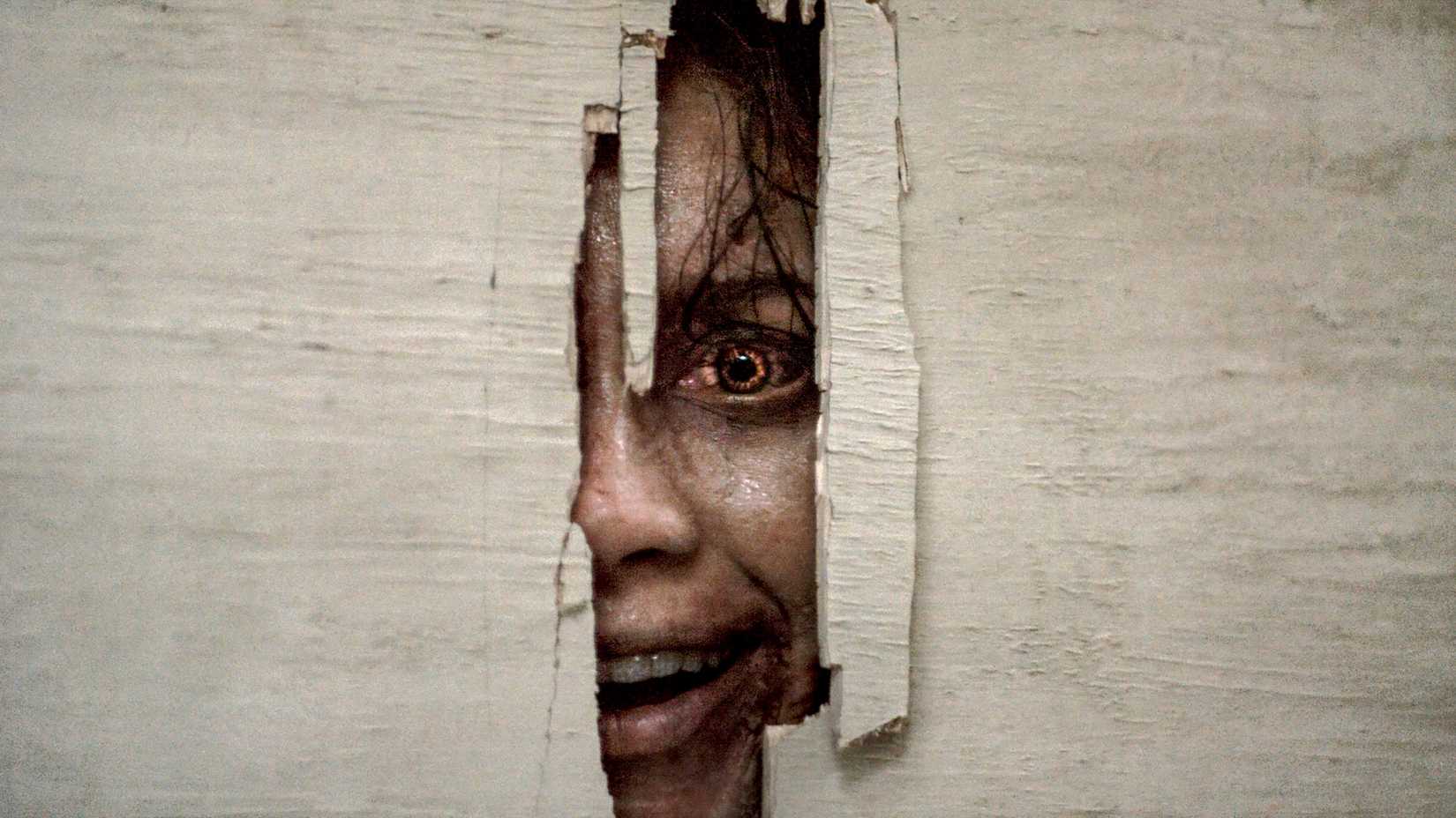 Luciane Buchanan's Thya smiling while looking through a hole in a door in Evil Dead Burn