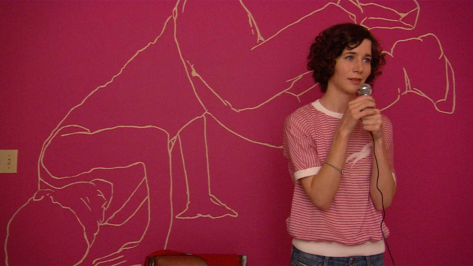 Miranda July performs in front of a red wall in Me and You and Everyone We Know