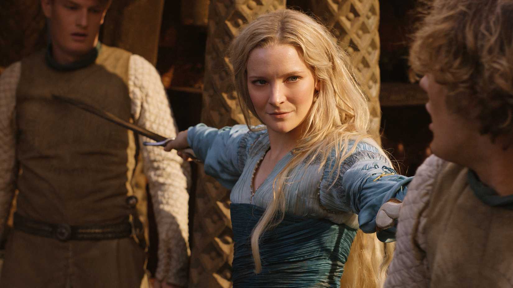 Morfydd Clark as Galadriel holding two attackers at swordpoint in The Rings of Power.