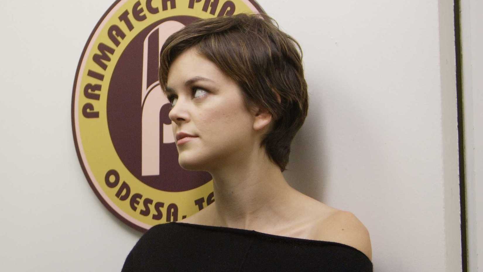 Eden McCain standing next to a wall with the Primatech logo