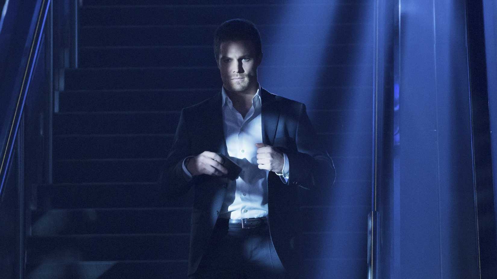 Oliver Queen stands in front of a staircase in Arrow season 1 episode 1
