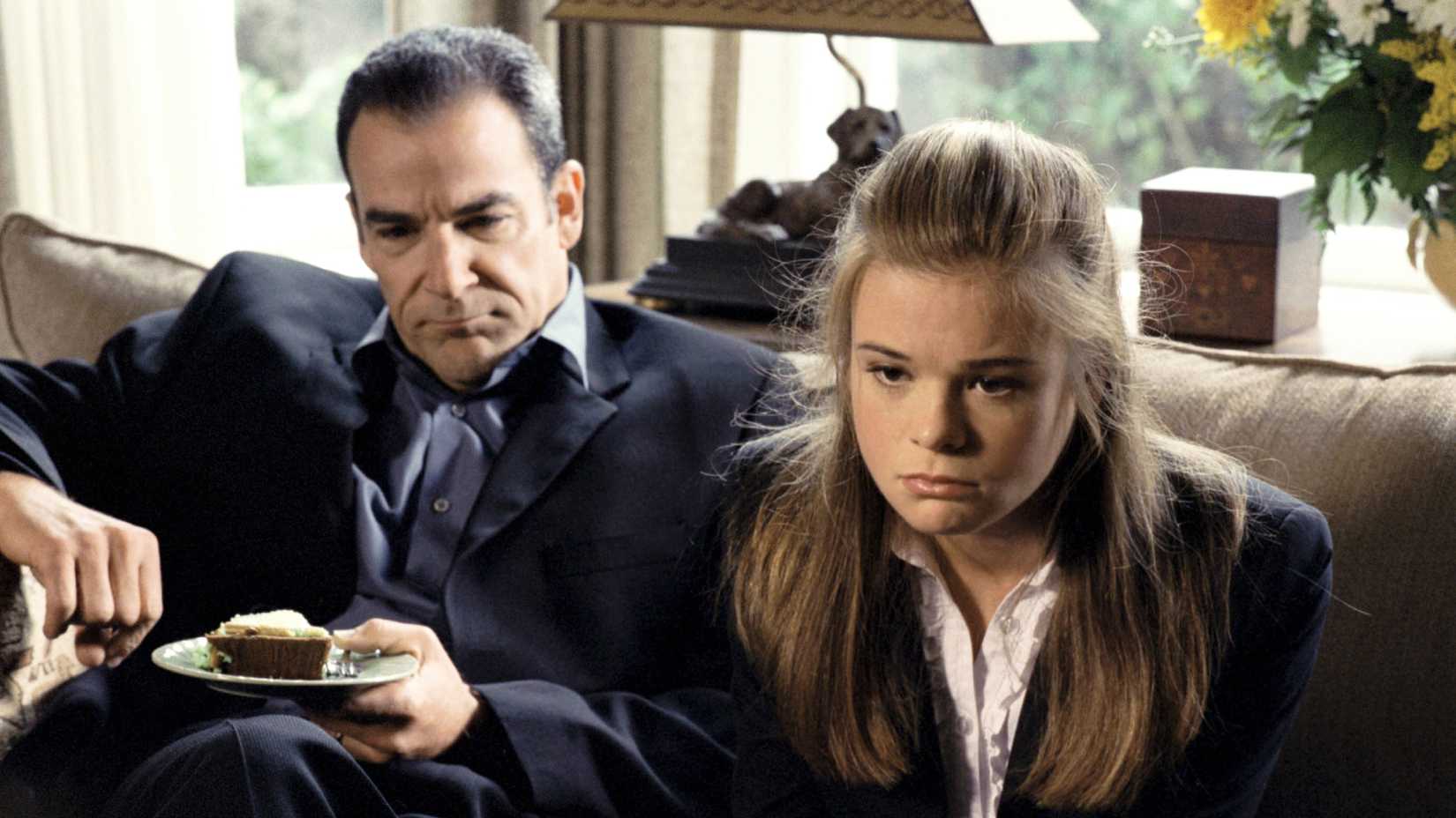 Rube holds a piece of cake and George looks down sadly while they sit on a couch in Dead Like Me