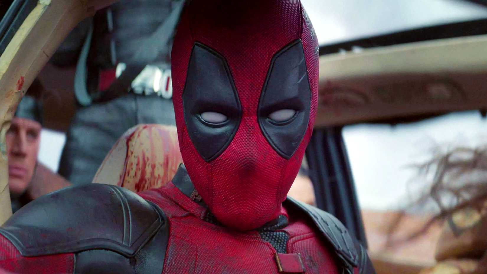 Ryan Reynolds' Deadpool looking at the camera in a car with other heroes in Deadpool & Wolverine