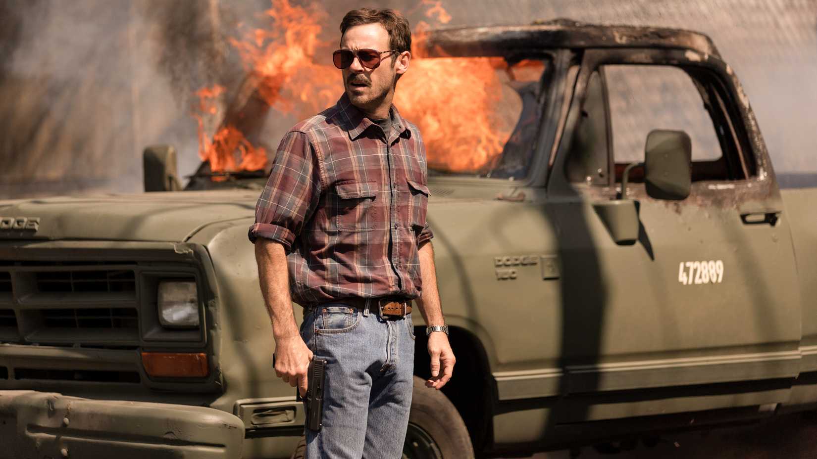 Scoot McNairy as Walt Breslin in front of a burning car in Narcos Mexico