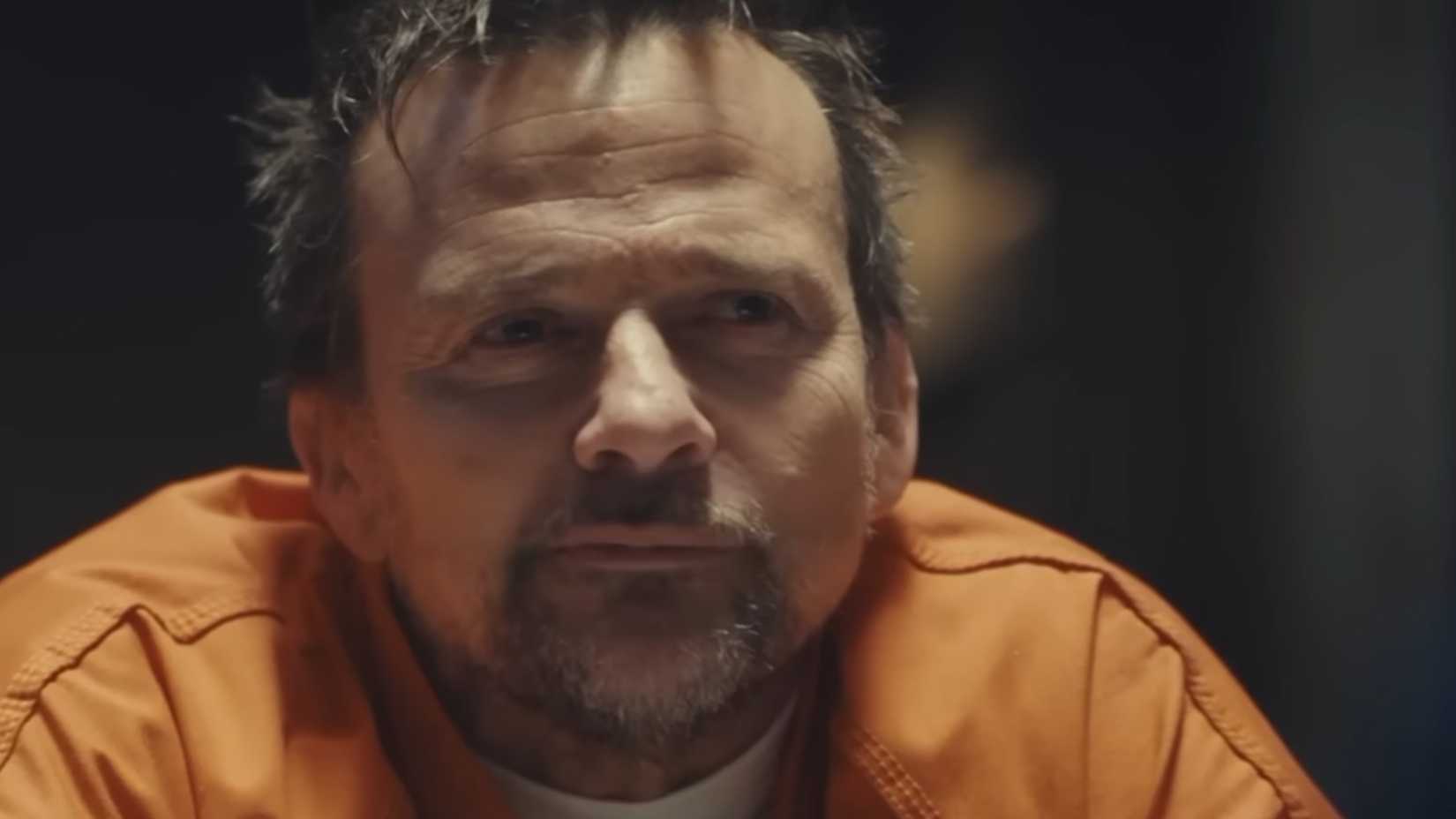 Sean Patrick Flanery smirking in an orange prison shirt in Nefarious