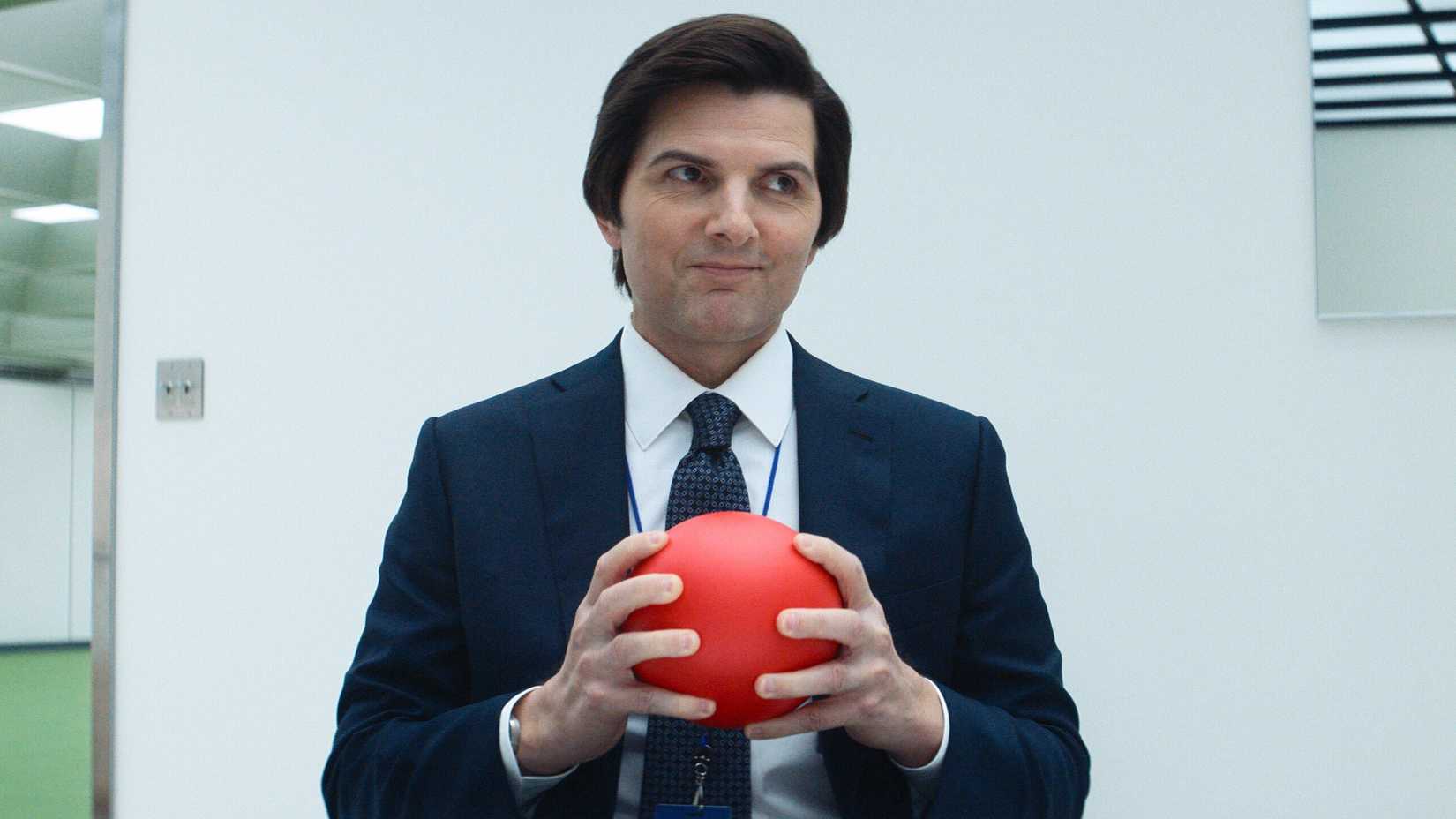 Adam Scott holding a red ball and smiling in Severance