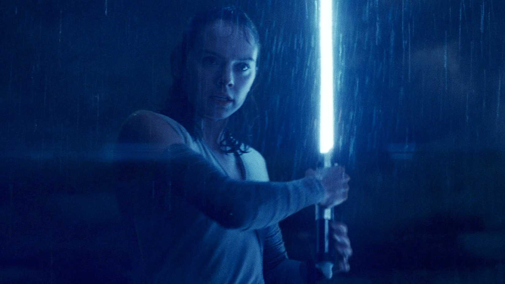 Daisy Ridley as Rey holding her blue lightsaber in the rain in Star Wars: Episode VIII - The Last Jedi