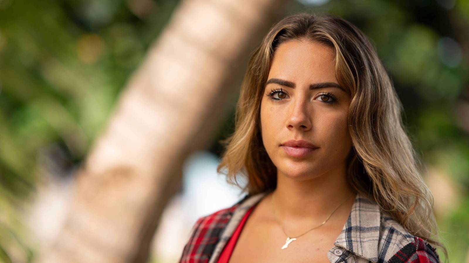 A still from Survivor 50 featuring Dee Valladares in front of a palm tree.