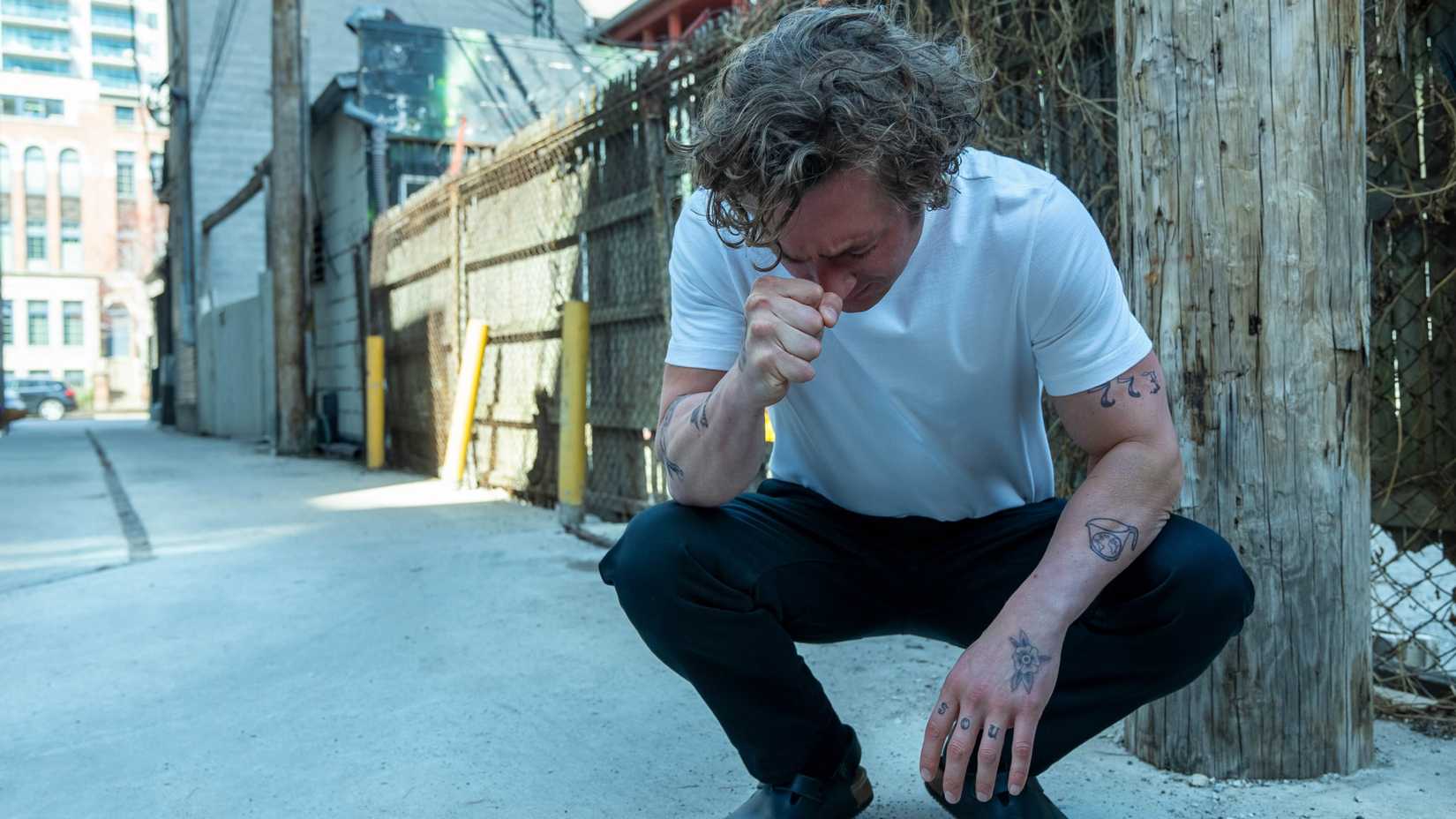 A still of Jeremy Allen White crouching on the ground in a white t-shirt and dress pants during The Bear season 2, episode 9.