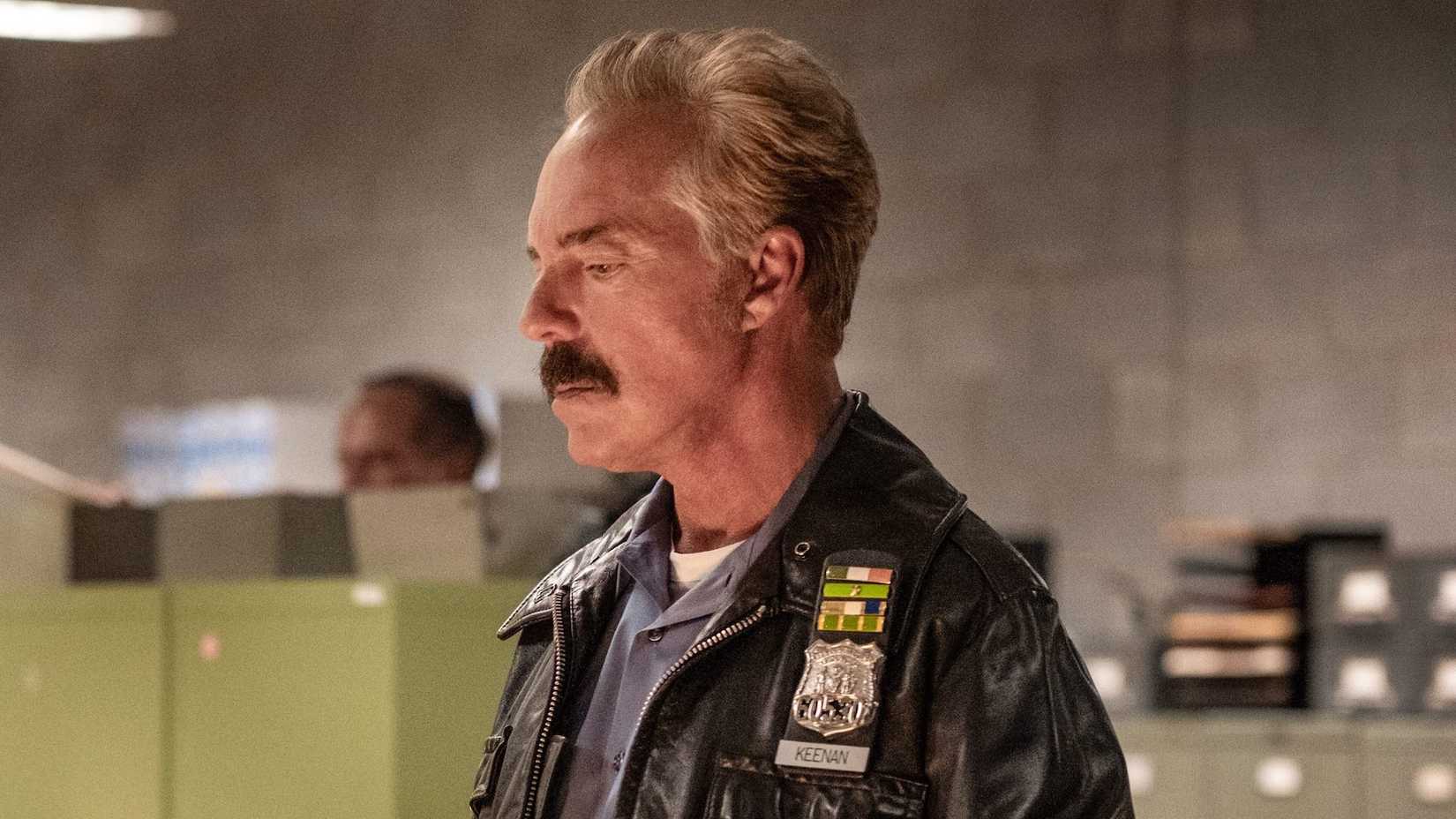 Titus Welliver wearing a 1980s-era police uniform inside a police station bullpen