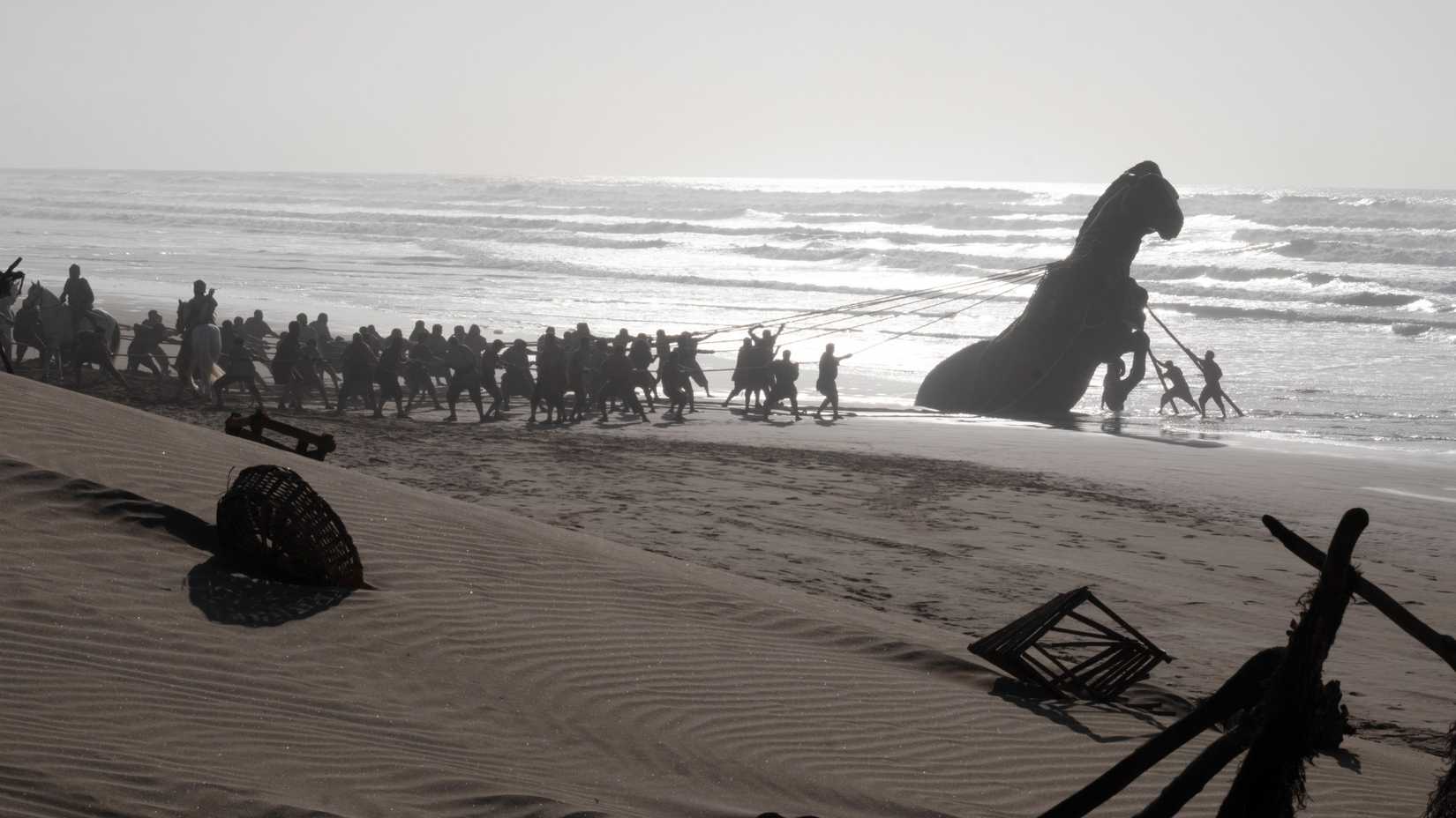 Trojans pulling the wooden horse out of the sand in The Odyssey