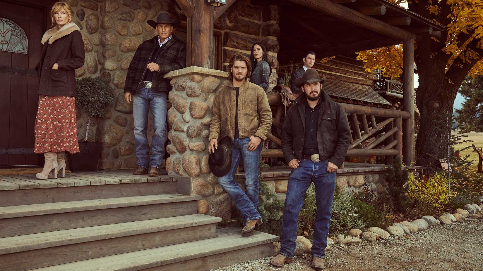 Yellowstone still featuring the Dutton family cast standing on the stone steps of the family home.