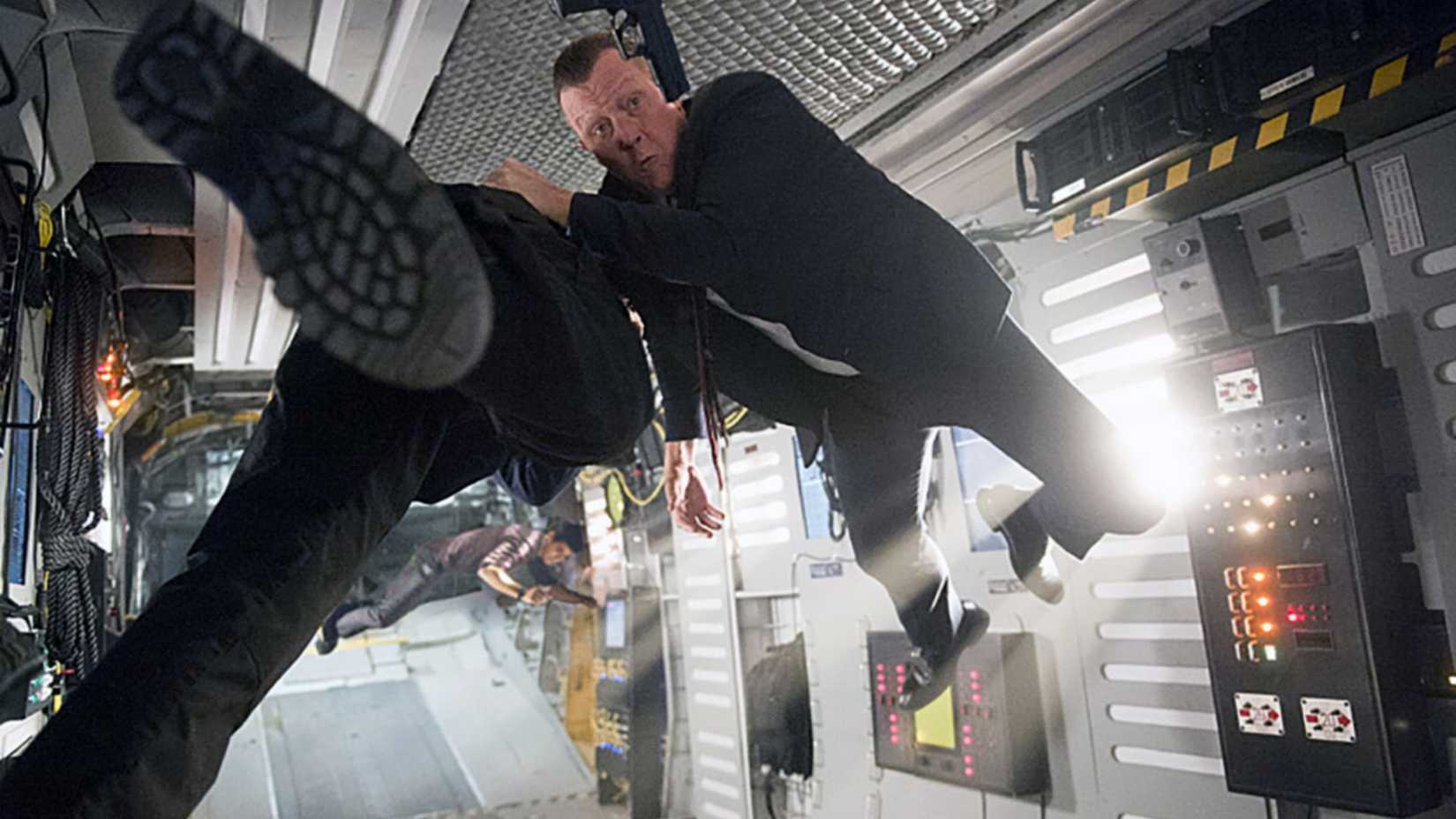Two men are tossed around a plane. A gun can be seen floating mid-air.