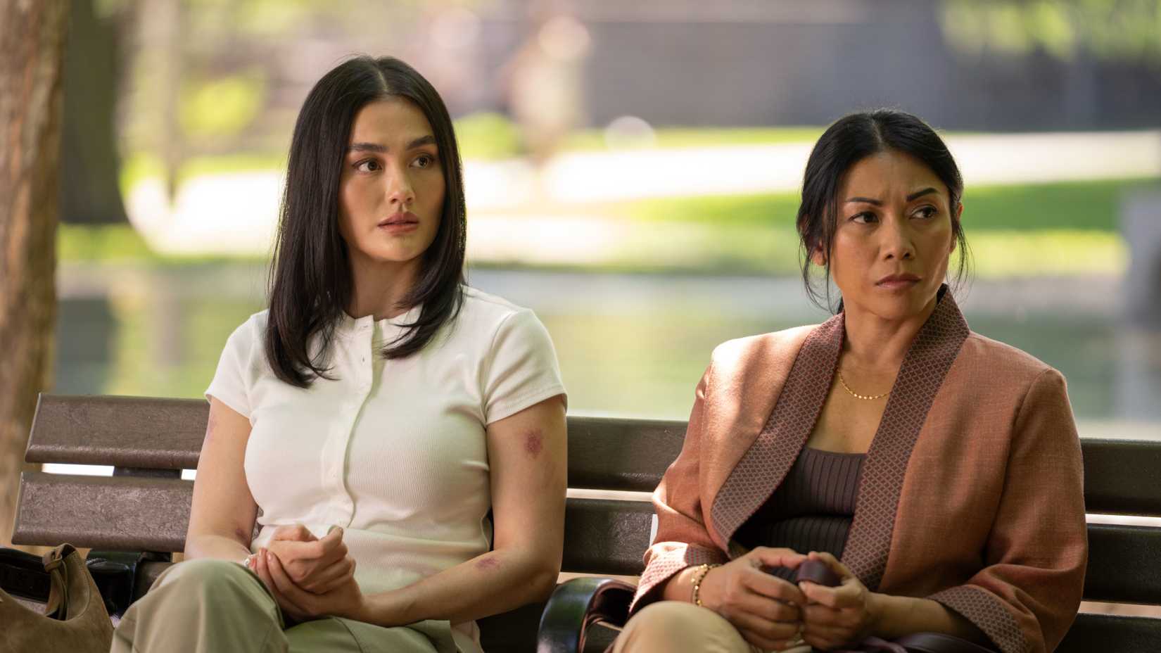 Agnez Mo and Anggun sitting on a bench in a park in Reacher season 4