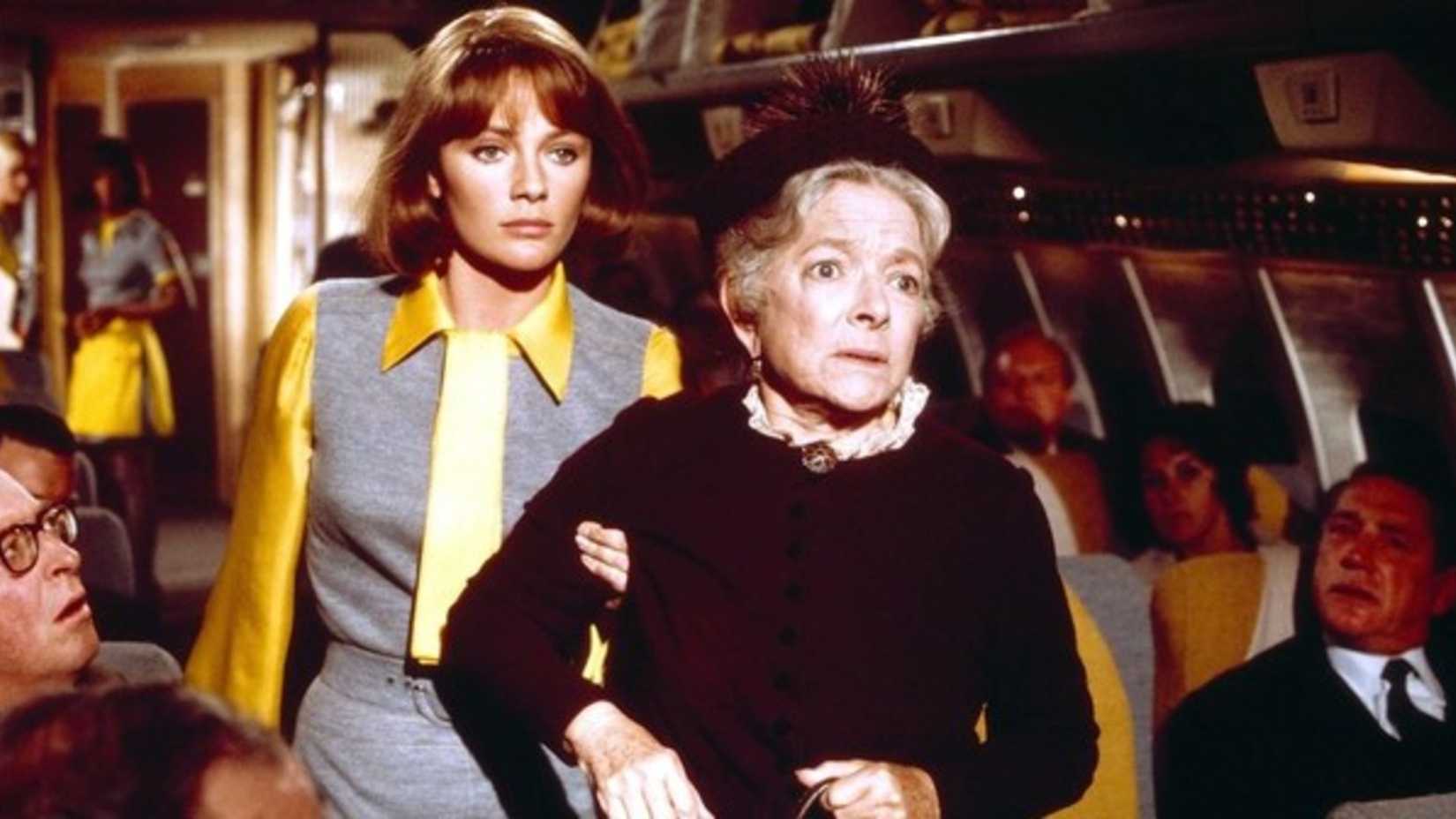 A stewardess helps an older woman down the aisle in Airport