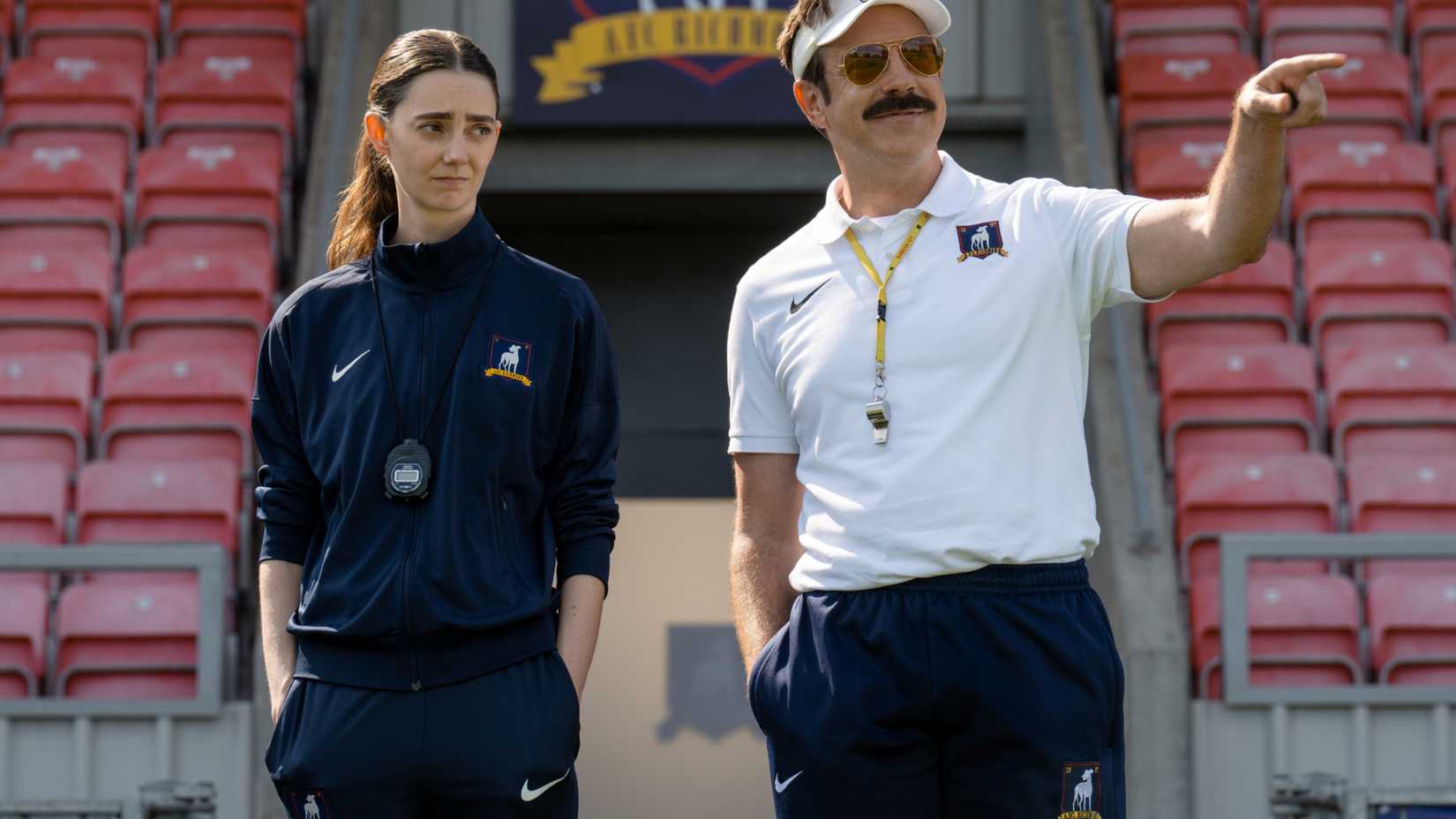 Alice Chilton (Tanya Reynolds) frowning as Ted Lasso (Jason Sudeikis) smiles and points in Ted Lasso