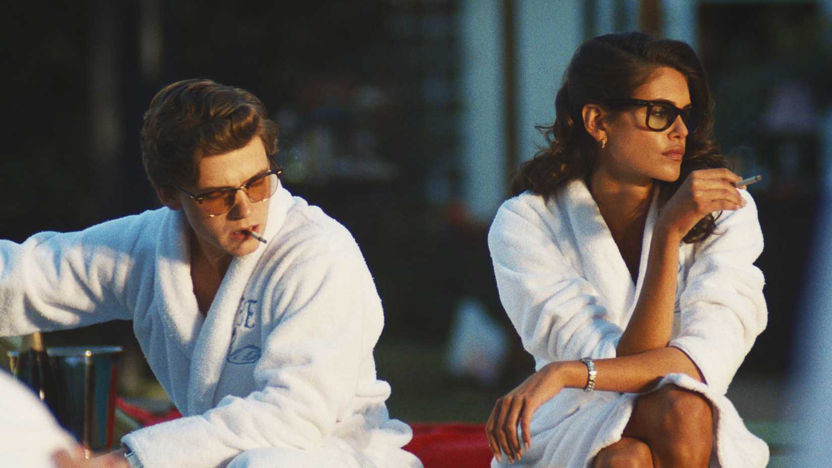 Bret and Susan sit next to each other on a lounge chair in bathrobes smoking cigarettes in The Shards
