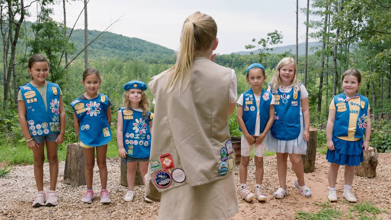 A girl scout addressing a line of junior scouts in Cookie Queens