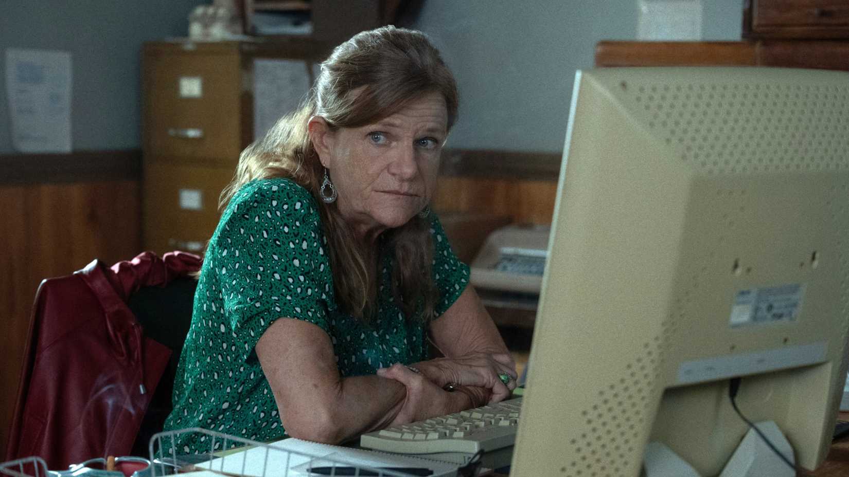 Dale Dickey sits at her desk looking glum in a scene from Widow's Bay season 1