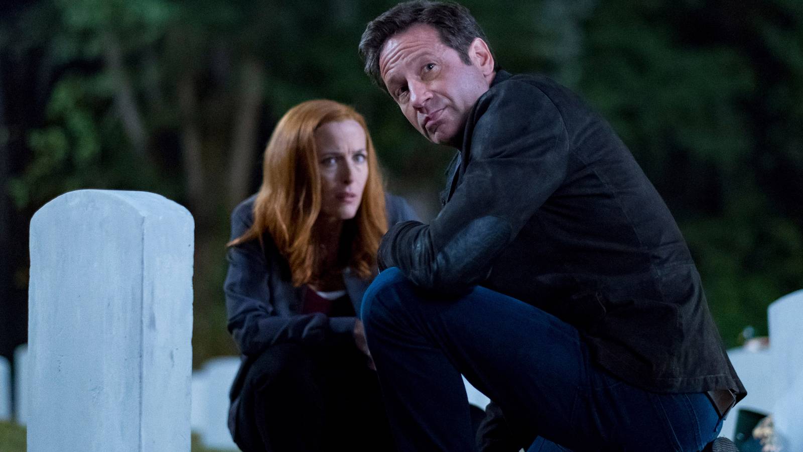 David Duchovny's Mulder and Gillian Anderson's Scully squatting in front of a gravestone in The X-Files