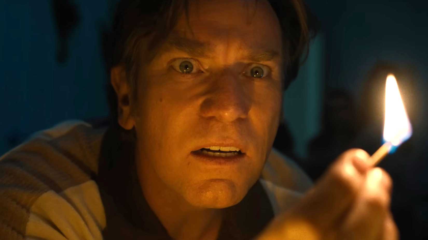 Ewan McGregor's Greg looking scared while holding a match in front of his face in The End of Oak Street