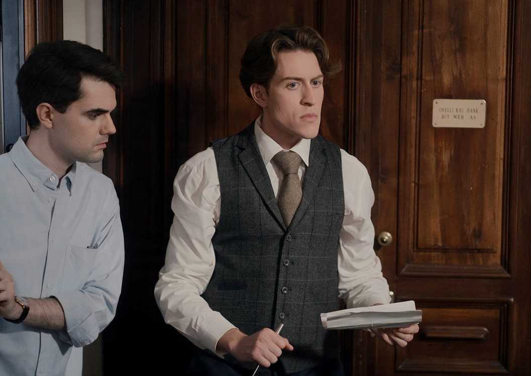 Watson looking at Sherlock, who's holding a pen and paper, in Moriarty Rising