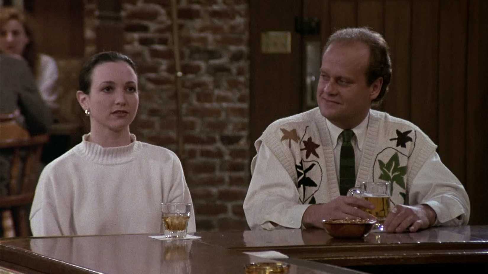 Frasier (Kelsey Grammer) smiling at Lilith (Bebe Neuwirth) at the bar in Cheers.