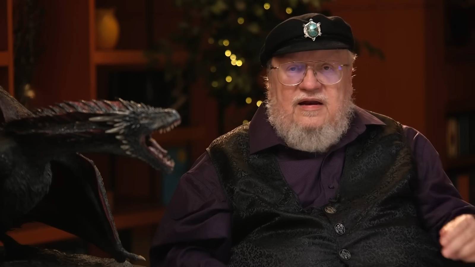 George R.R. Martin speaks next to a figure of Drogon from Game of Thrones.