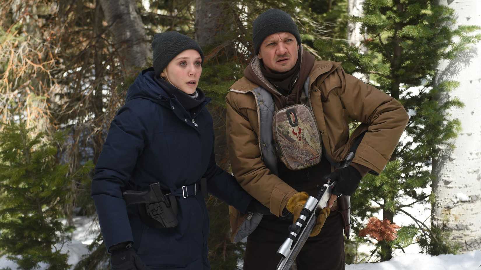 Jeremy Renner as Cory Lambert with a gun standing with Elizabeth Olsen as Jane Banner in Wind River