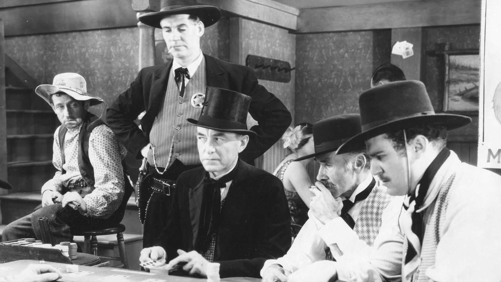 Men sit and stand around a card table in Law and Order