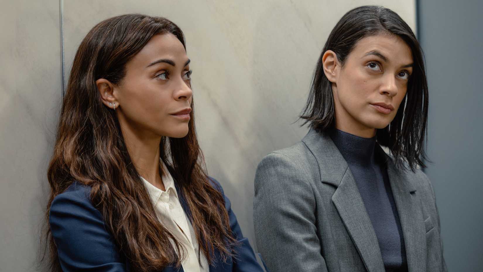Joe (Zoe Saldaña) and Cruz (Laysla De Oliveira) standing against the wall in suits in Lioness season 3
