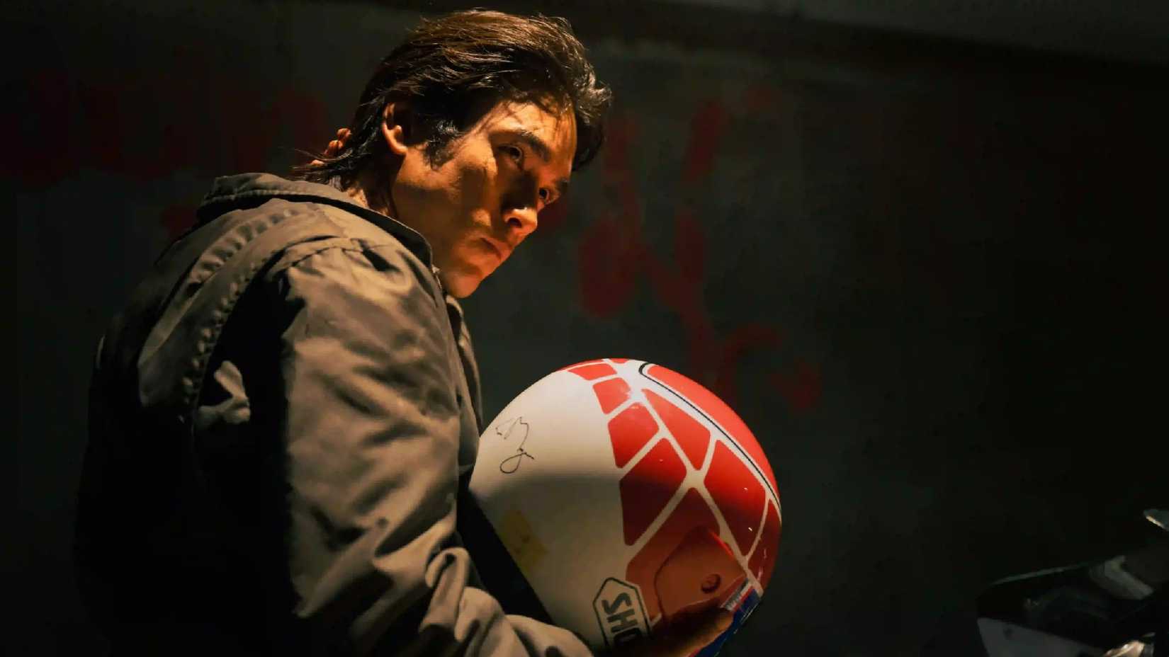 Num is holding his helmet in The Debt Collector