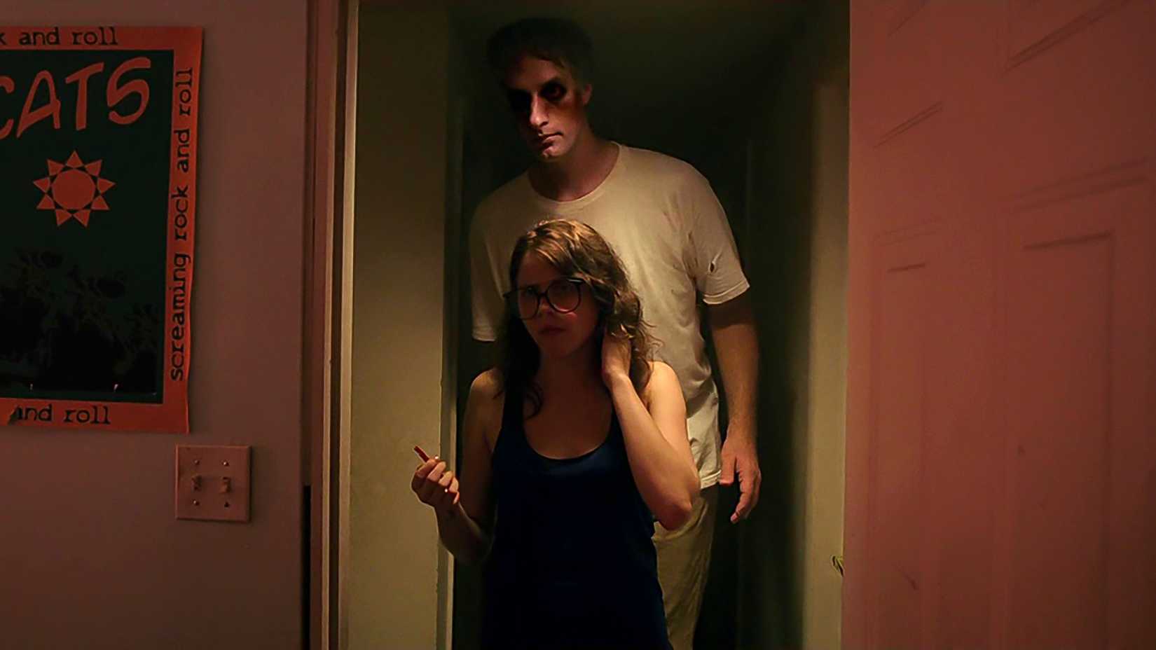 Olivia Luccardi's Yara looking confused with the Tall Man standing behind her in It Follows