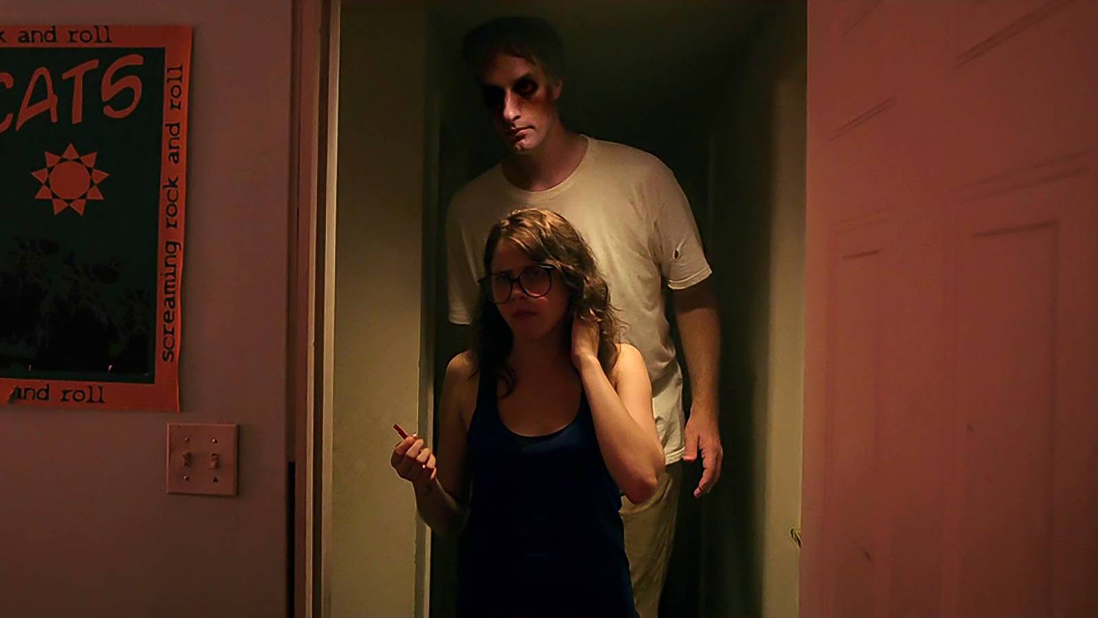 Olivia Luccardi's Yara looking confused with the Tall Man standing behind her in It Follows