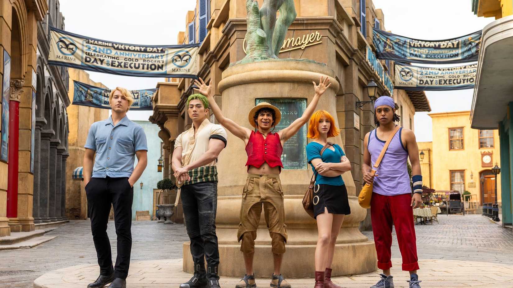 The cast of One Piece standing in front of a statue
