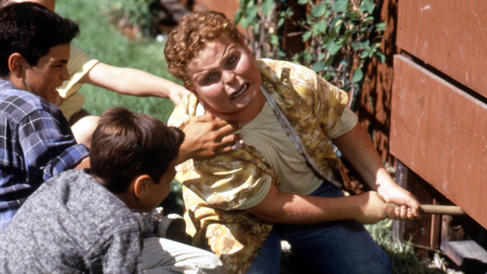 Patrick Renna looks distressed while struggling to retrieve a baseball bat from under a fence in a scene from The Sandlot