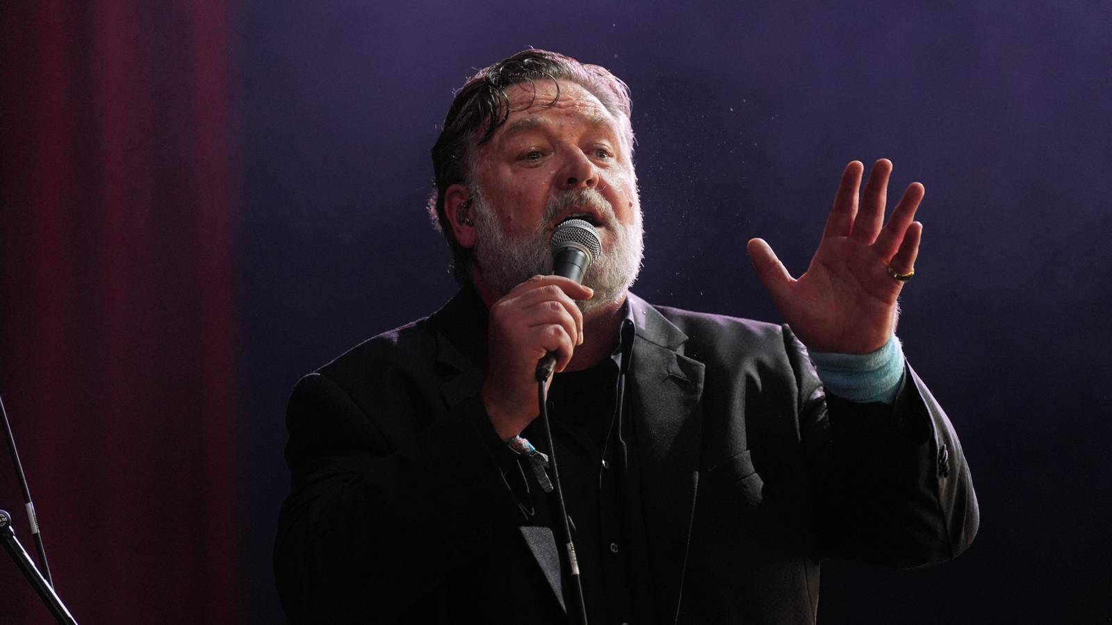 Russell Crowe gestures as if telling a story during an on-stage appearance