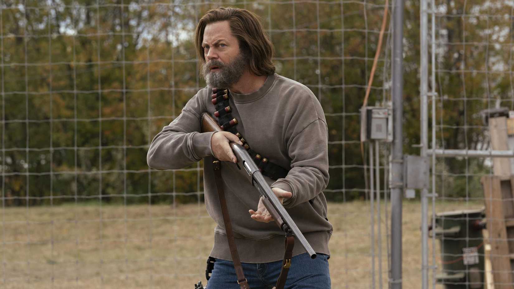 Bill (Nick Offerman) holding a gun next to a fence in The Last of Us.