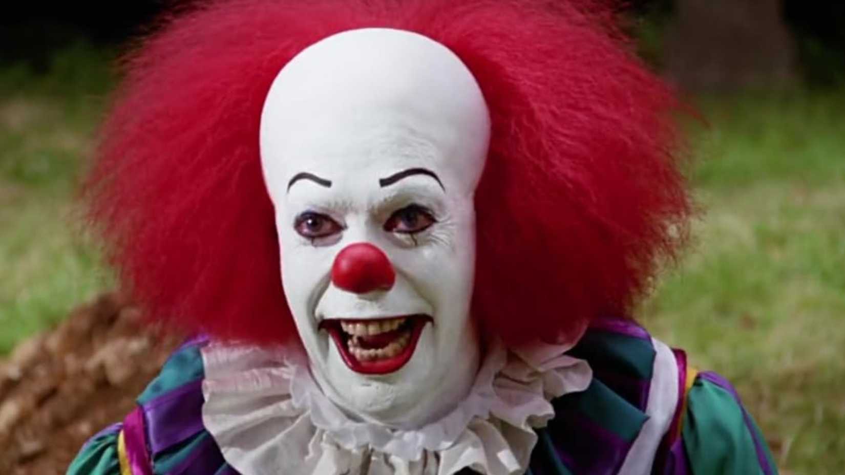 Tim Curry as Pennywise smiling in It 1990 miniseries