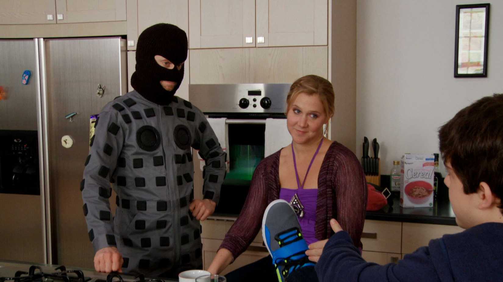 Two characters, one in a balaclava, talking to a younger boy in a kitchen in Delocated