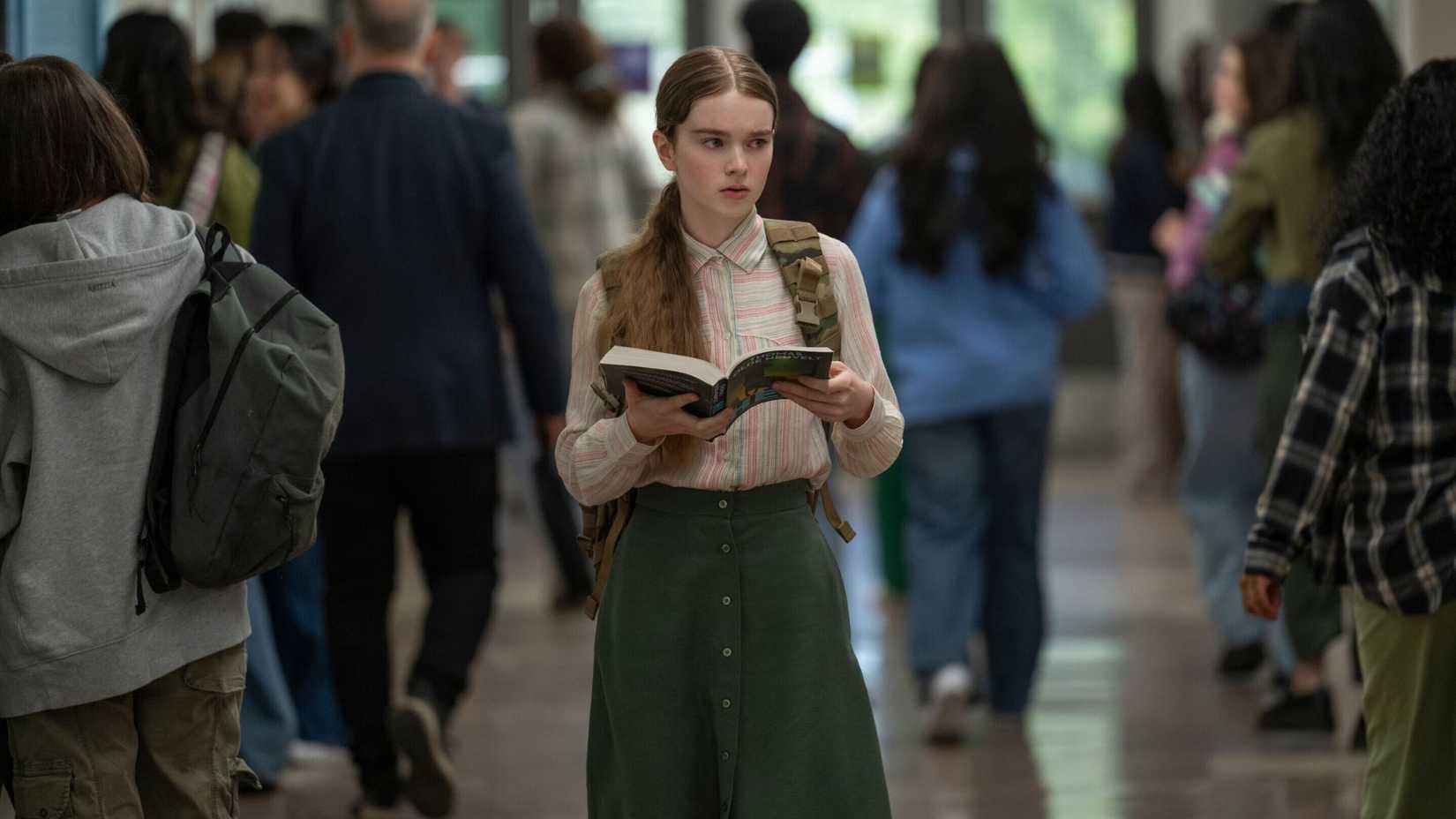 Carrie walking through the school hallway reading a book