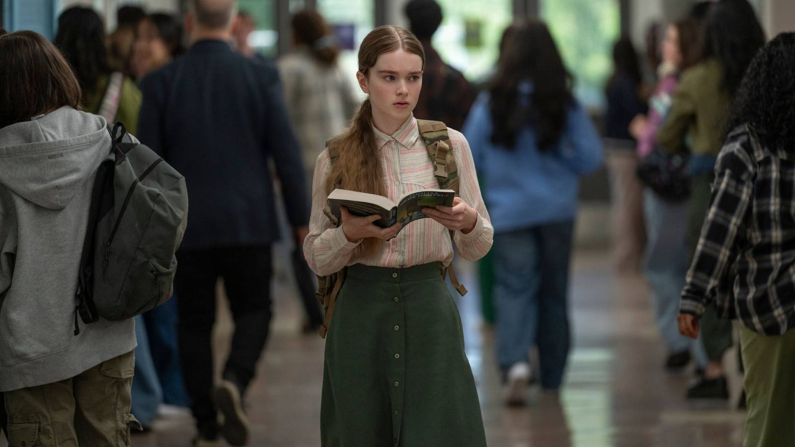 Carrie walking through the school hallway reading a book
