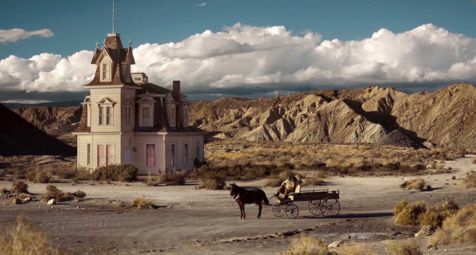 Wide shot of a gothic house in the middle of a rocky desert landscape with a horse and buggy parked in front of the house in Dead Souls
