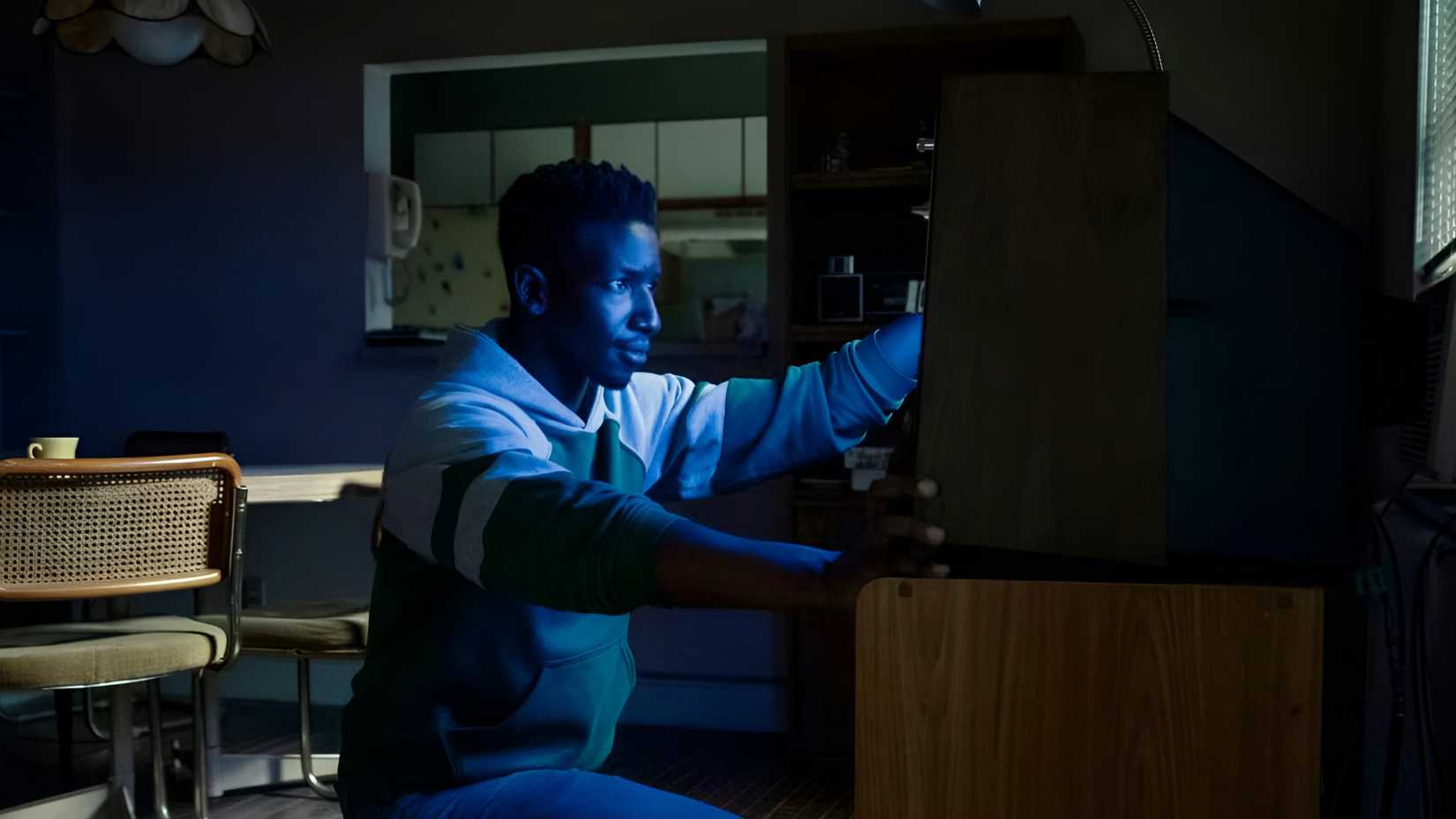 Mamoudou Athie‘s Dan Turner sitting in front of a TV’s blue screen in Archive 81