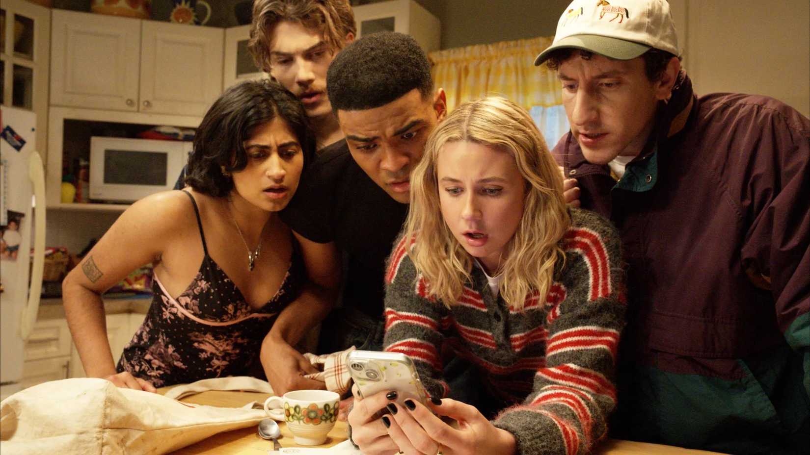 Issa, Paul Baker, Anton, and Samir crowd around Billie looking at her phone in Adults.
