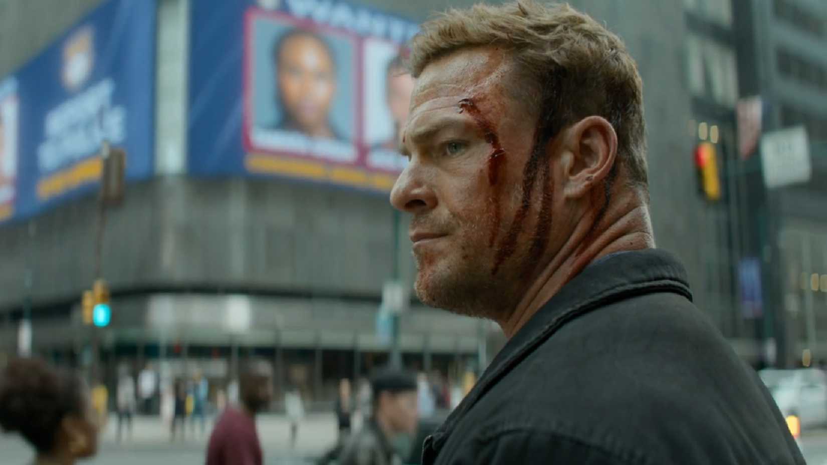 Alan Ritchson as a bloody Reacher in front of a wanted poster.