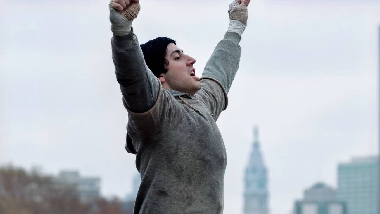 Anthony Ippolito as Sylvester Stallone with his arms up in I Play Rocky