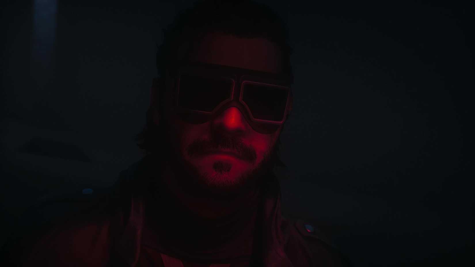 Close-up on a man bathed in red light, wearing goggles.