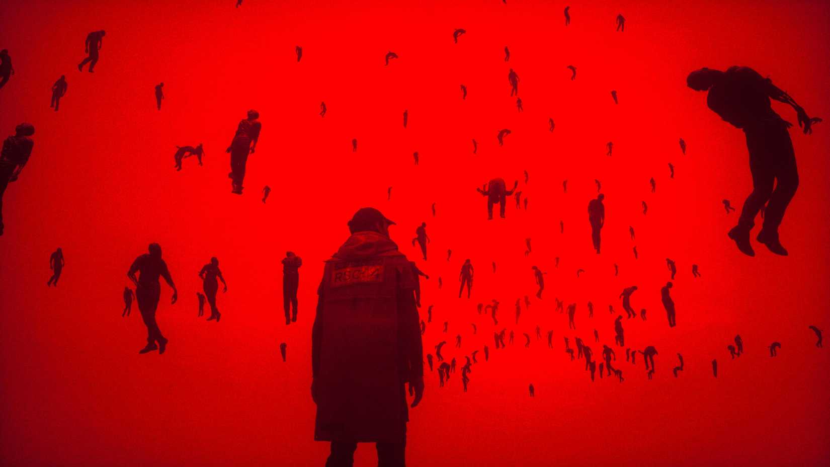 Man in a frock and baseball cap standing in a vibrant red void, surrounded by suspended bodies.